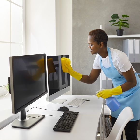 woman cleaning office screens using yellow cloth in blue apron